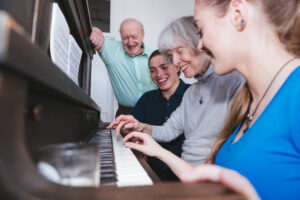 アップライトピアノを囲んで笑顔で演奏する人たち